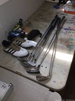 View showing the golf shoes, irons, putters, golf balls and glasses arranged on a table.