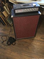Side and front view of the red textured speaker cabinet with amplifier head on top and cords laid in front.