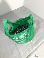 Green reusable shopping bag containing a large collection of multicolored glass marbles, viewed from above.