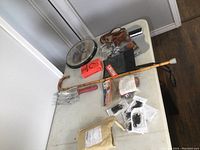 Various items including bamboo cane, gardening scoop, clipboard, Bluetooth gadgets and dog collar on table.