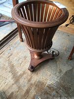 Full view of the wooden planter stand showing the circular open slat basket design and the smooth rim