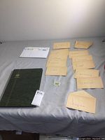 Photo showing stamp album, multiple labeled envelopes and a single loose stamp on a gray surface.