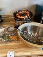 Photo showing multiple mixing bowls nested, copper bundt pan, double boiler pot, and kitchen utensils on countertop.