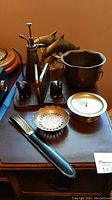 Photo showing the group of brass items on a wooden table including bookends, flower pot, candle holder, letter opener with sheath, and flower mister.