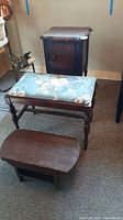 Overall view of the small dark wooden cabinet, blue floral upholstered bench, and small wooden footstool grouped together on floor.