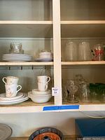 Corelle plates, bowls and floral cups on shelves with clear drinkware and glasses