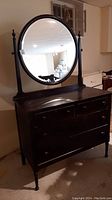 Front view of the dark wood vintage dresser with attached round bevelled mirror and four drawers.