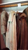 Three fur items hanging: two jackets and one shoulder wrap in beige cream, medium brown and light beige/pinkish tones.