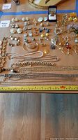 Full spread view of assorted pearl, rhinestone, and metal earrings, brooches, bracelets and necklaces on a table with a measuring tape showing sizes from about 7 to 16 inches.