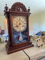 Front view of the wooden mantel clock showing round face with Roman numerals and decorative top with finials.