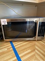 Full view of the stainless steel microwave sitting on a wooden countertop, showing the front and control panel.