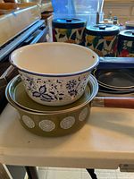 Two sauce pans stacked, one white enamel with blue floral design, one green with white geometric pattern and wooden handle.