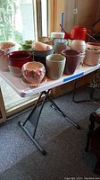 Full view of all twenty assorted ceramic flower pots on table, various colors and sizes from 4 to 7 inches.