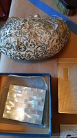 Photo showing small evening bag with metallic floral pattern and mother of pearl compact in a box with a velvet pouch and compact notepad to the side