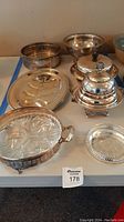 Lot of silverplate serving pieces including relish dish with glass insert, platters, covered dishes, bottle coaster, and round dishes.