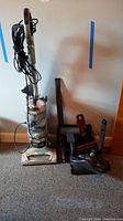 Full view of Shark upright vacuum with attachments and cordless handheld vacuum on floor against wall