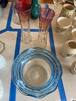 Two cranberry glass vases with gold floral/leaf details near the rim, standing tall and slender. Bubble glass vase with blue swirled rim and air bubbles in the glass body placed in front.