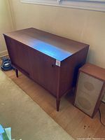 Front view of vintage stereo console with sliding doors closed, and separate speaker standing next to it