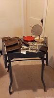 Full view of table displaying all items in the lot including vintage travel mirror, cases, postcards, and notepad