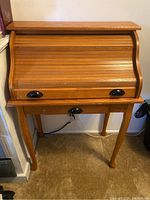 Full front view of antique wooden roll-top desk showing wooden slats on roll-top and drawer with black handles, curved legs, and natural wood finish.