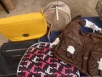 Photo showing five handbags: yellow, round beige, black Kelly Moore, brown Ampere Creations, and black Dana Buchman. Most have tags; Dana Buchman is lightly used.