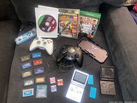 Wide view showing all gaming items including 2 handhelds, controllers, game cartridges, and game cases.