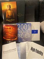 Collection of movie press kits laid out on couch, titles visible: Kundun, Silver Linings Playbook, Signs, Universal Movie Preview 2001, Pirates of the Caribbean, High Fidelity