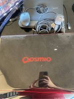 Top view of Toshiba Qosmio X505-Q860 laptop closed lid with red Qosmio logo visible. Wired mouse, Belkin cooling fan and cables also visible.