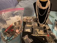 Overview of mixed costume jewelry in plastic bags, loose pearls on table, and necklaces displayed on black bust.
