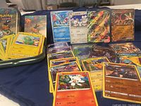 Photo showing various Pokémon cards laid out near a Pokémon-themed tin with Pokémon artwork including Scorbunny card and some foreign language cards.