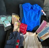 Photo showing all items from the bundle including blue polka dot bathing suit, packages of Love Your Assets shaping tights, bodysuits, and socks on black background
