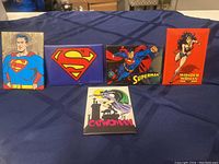Five superhero magnets on table including Superman full-body, Superman emblem, Superman action pose, Wonder Woman, and Catwoman.