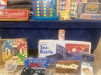 Overall view of various vintage games including Rummikub box set, Connect 4, Password, Sea Battle board, dominoes, peg games, and Trouble game