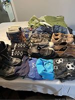 View of assorted clothing and footwear spread on a bed including winter boots, sandals, t-shirts, shorts, and a green winter coat for women.