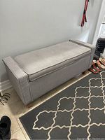 Front and angled side view of the rectangular cloth upholstered entrance bench showing cushioned lid and wooden legs.