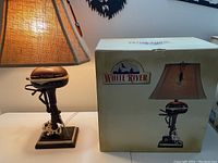 Photo of one lit White River vintage outboard motor table lamp and its original box beside it showing box graphics and branding.