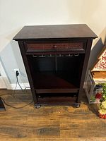 Front view of the dark wooden wine cabinet showing the drawer, built-in glass rack, open storage, and caster wheels.
