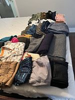 Full assortment of folded clothes including pants, sweaters, scarves, gloves and hats laid out on bed