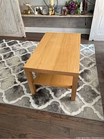 Wooden coffee table placed on patterned rug viewed from an angle showing the side and lower shelf.