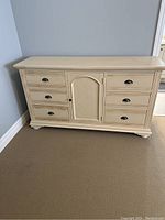 Front view of the wooden dresser showing six drawers and central cabinet door with dark metal cup pulls