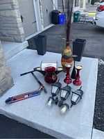 Lot items displayed on concrete patio - includes multi-colored vase, red candle holders, red glass vase, black outdoor lanterns, and metallic scooter.
