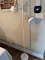 White floor lamp with two adjustable heads against wall near thermostat