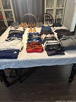 Full view of lot on table showing neatly folded shirts, pants, and six pairs of men's shoes in front.