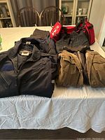 Photo of men’s jackets, fleece vest, coveralls, dress pants, and gym bags on table