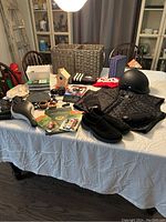 Wide shot of the lot items on a white tablecloth. Includes motorcycle helmet, jacket lining, shoes, gloves, golf books, bike seat, storage baskets, and various small items including electronics.