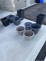 Overview of all nine plastic planters arranged on concrete surface near garage.