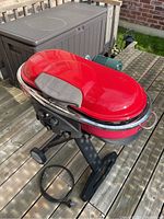 Red Coleman portable propane BBQ grill on a wooden deck, showing full body with wheels and folding legs.
