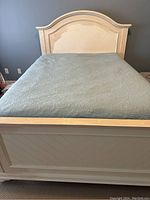 Front view of queen-size bed frame with paneled footboard and light blue bedspread