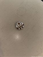 Close up photo of Queen's Silver Jubilee 1977 lapel pin showing gold crown, laurel wreath, and year '1977' on white background.