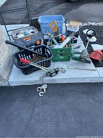 Wide view of assorted electrical and renovation supplies laid out on sidewalk including plastic crates, metal tools, and garden equipment
